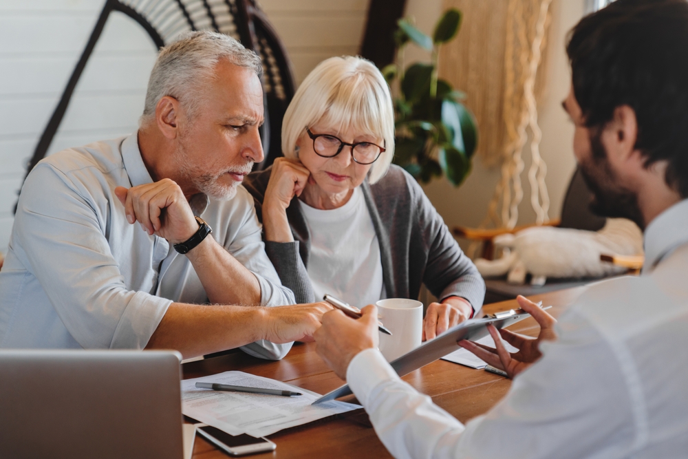 Older clients consulting agent, broker about house selling, medical insurance terms, trust fund investment, meeting at laptop in office. Senior couple discussing wills with lawyer, solicitor, notary.