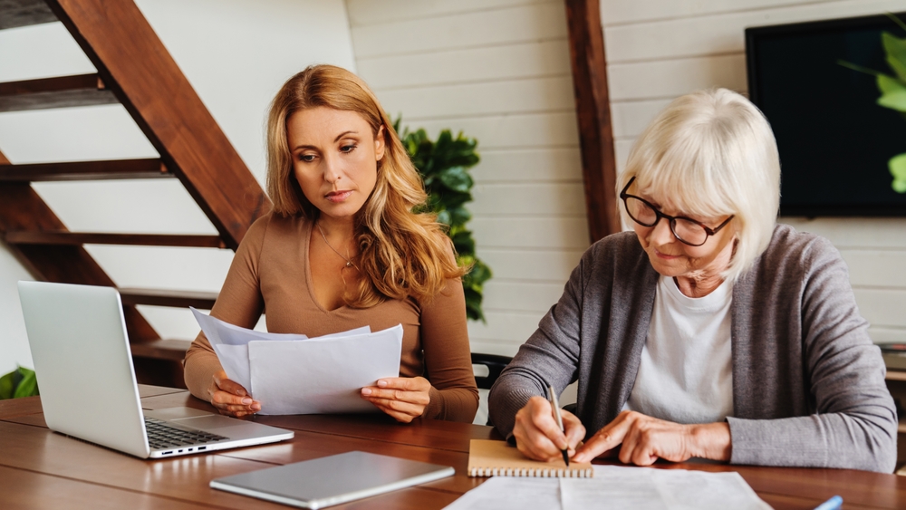 What Does Power of Attorney Mean? Senior woman with help of her daughter making bills at home, paying loan, debt, filling in medical insurance, mortgage documents, health insurance.