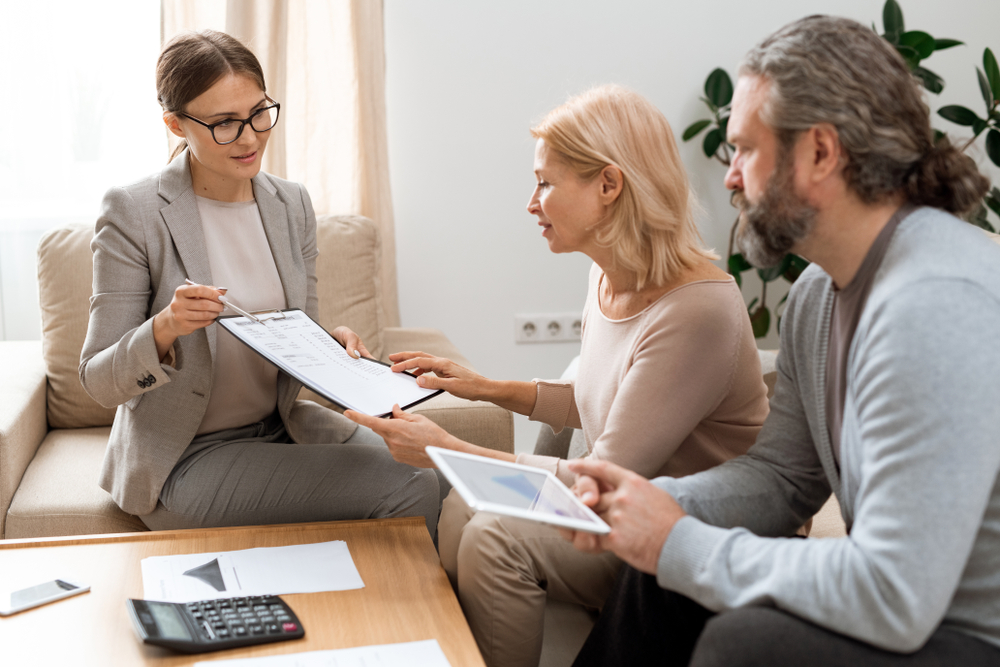 YoungRealEstateAgentWithDocumentPointingAtSumOf Real estate professional discussing property documents with a client during a financial planning consultation.