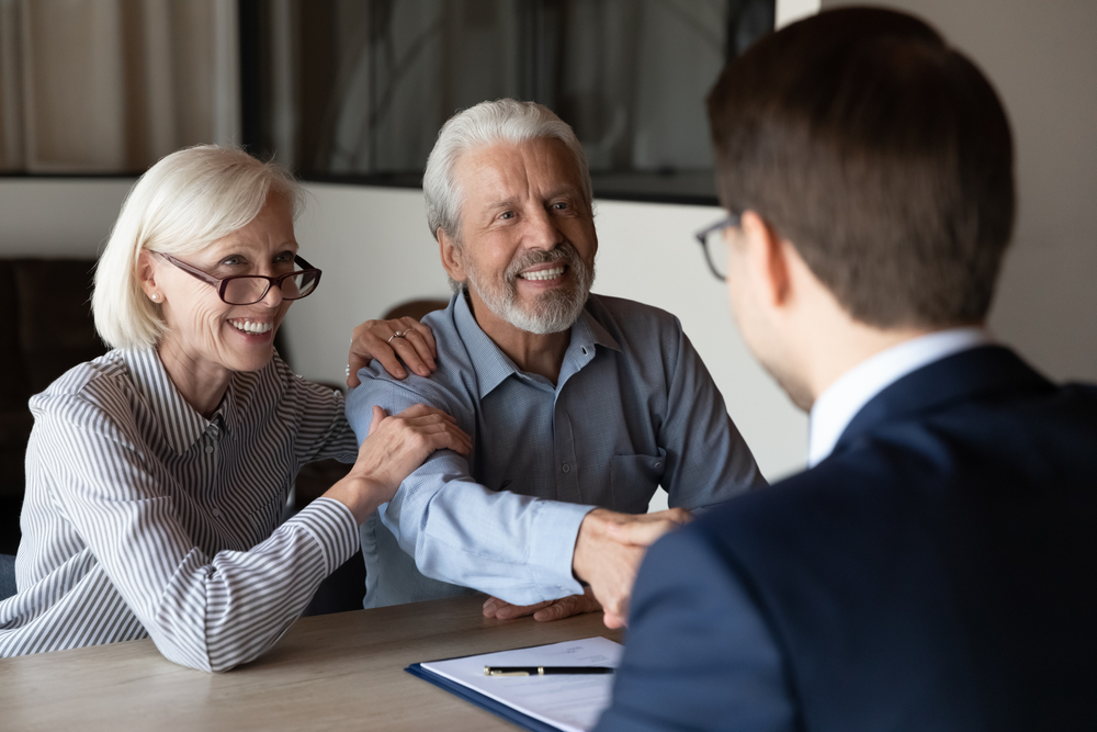 SmilingOlderCaucasianManAndWomanClientsShakeHandGreeting Older couple meeting with a professional to discuss estate planning
